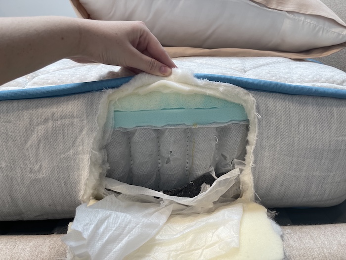 A closeup of the side of the Bear Cub mattress. The fabric has been cut open, showing a bottom layer of springs and two top layers of foam.