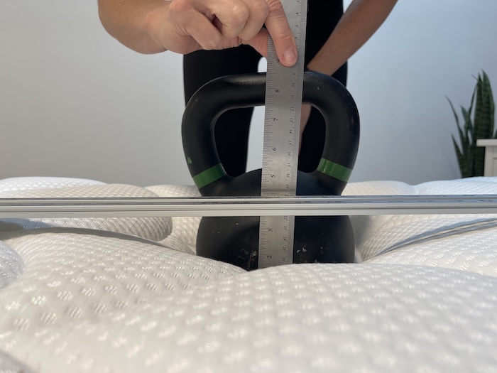 A kettlebell resting on top of the DreamCloud mattress. Someone is measuring its sinkage with a ruler.