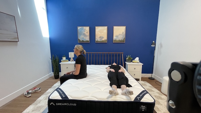 A woman sits on the edge of the DreamCloud mattress while another woman lies next to her.
