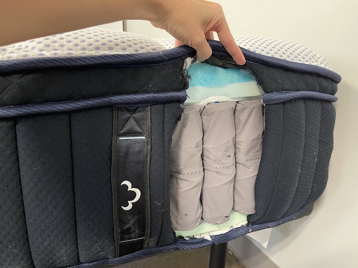 A closeup of the side of the DreamCloud Premier Hybrid mattress. A cross section has been cut out to reveal the bed's layers.