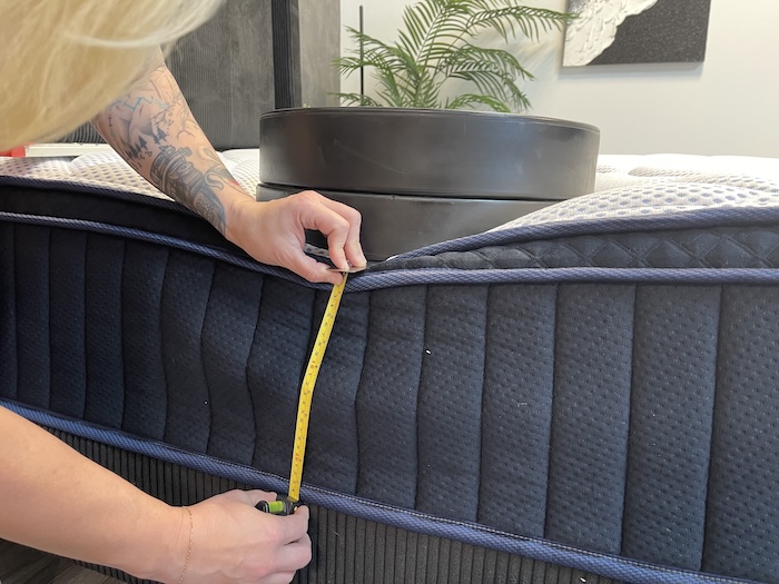 A closeup of a stack of weights resting on the DreamCloud Premier Hybrid mattress. A woman is measuring the sinkage with a tape measure.