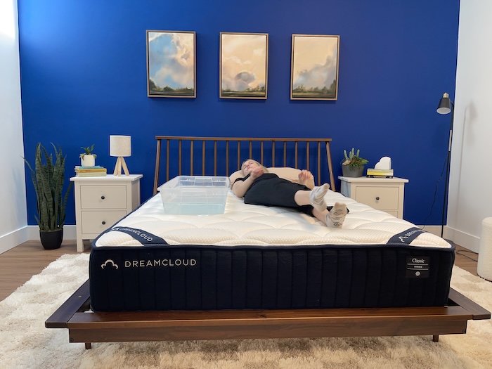 A woman lying on the DreamCloud mattress next to a plastic bin full of water.