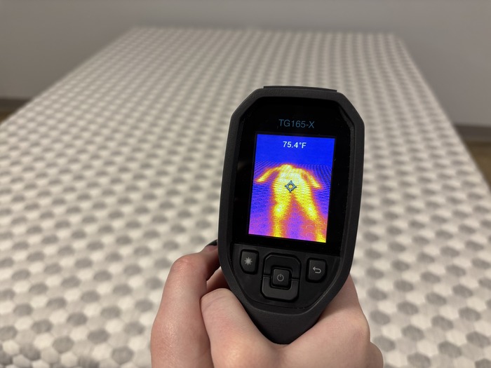 A closeup of someone pointing a thermal gun at the soft side of the Layla to take its temperature after someone has rested on it for 5 minutes. The screen reads 75.4 degrees.