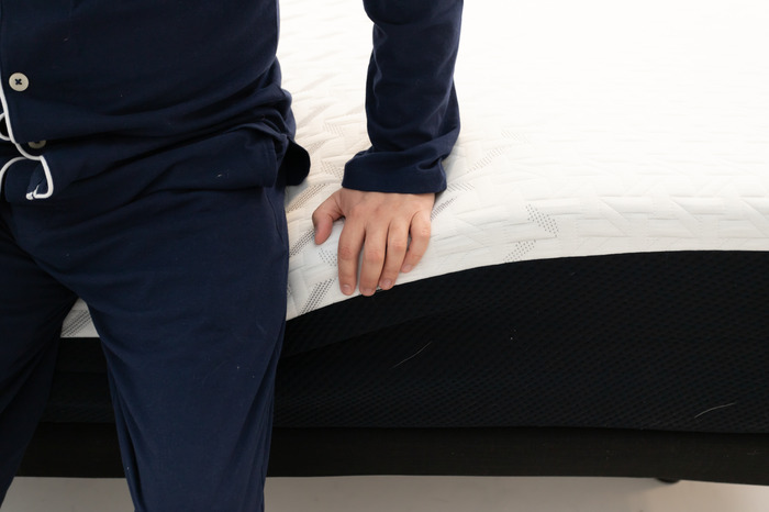 A close-up image of someone sitting on the edge of the Nectar mattress to test its edge support.