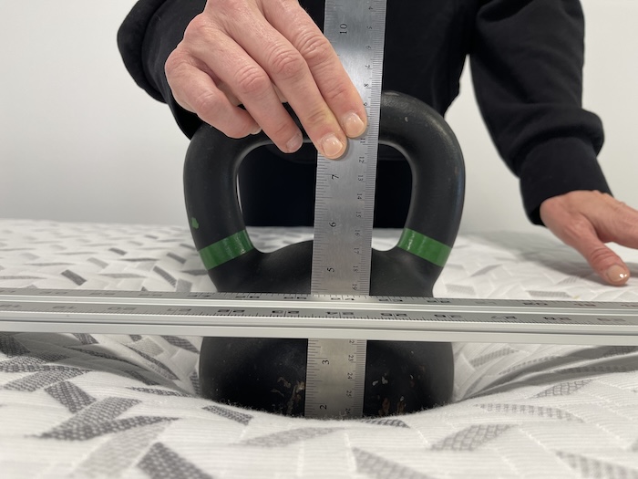 A kettlebell sitting on top of the Nectar. Someone is using a ruler to measure its sinkage.