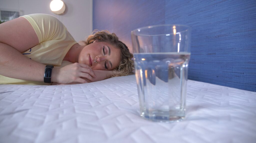A woman sleeps next to a glass of water on a Nectar Luxe Hybrid mattress.