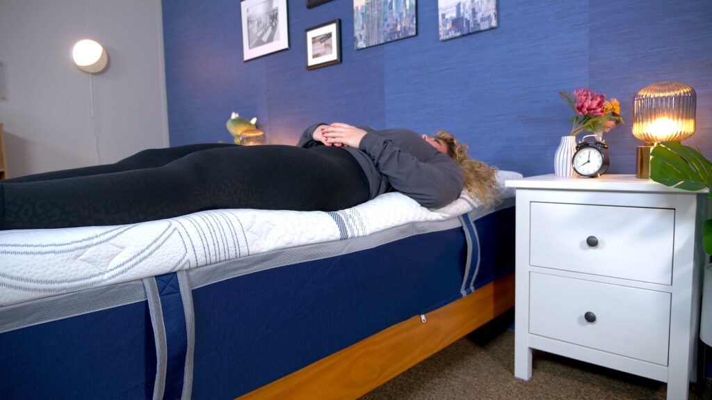 A woman lying near the edge of a mattress to test its edge support.