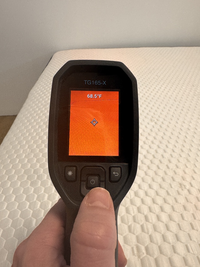 A closeup of someone aiming a thermal gun at the Brooklyn Bedding Aurora Luxe to get its resting temperature. The screen reads 68.5 degrees.