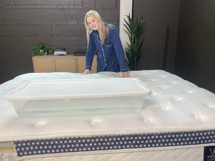 A woman standing next to the WinkBed and looking at a plastic bin full of water that's resting on the mattress.