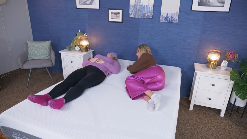 Two mattress testers lying on a bed and moving back and forth to test its motion isolation.