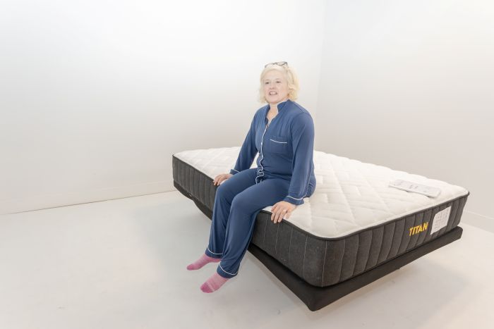 A woman sits on the edge of the Titan Plus mattress