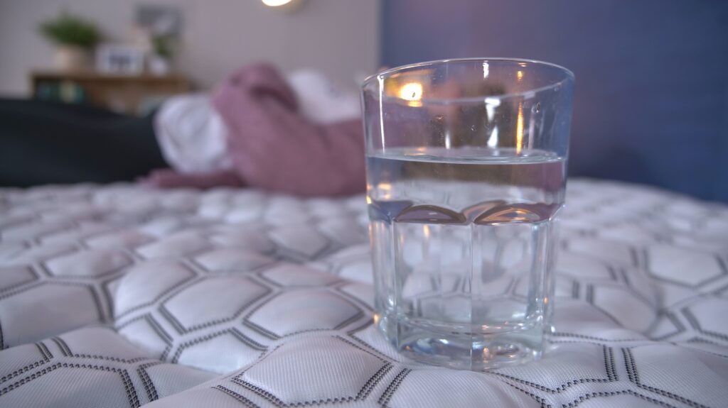 A woman lying next to a full glass of water on top of the Titan Plus Elite mattress.