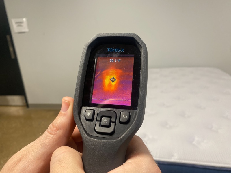 Someone holding a thermal gun and pointing it at the Silk & Snow Hybrid mattress to get its temperature.