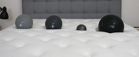 Four balls of different weights lined up on the surface of a mattress.